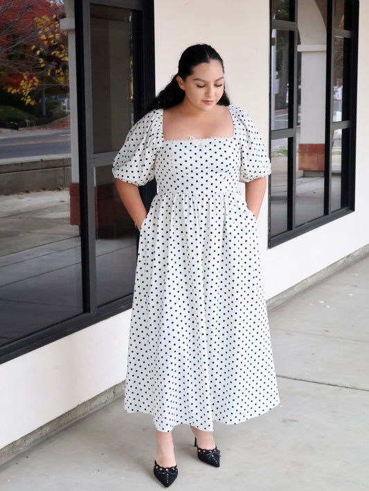 Woman wearing a white dress with black polka dots standing outside a building.